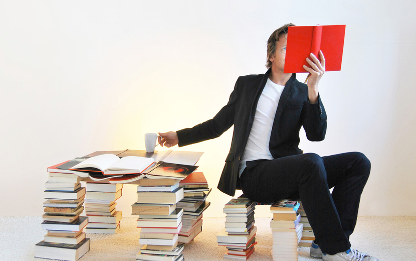 Ein Mann sitzt auf einem Bücherstapel und liest ein Buch