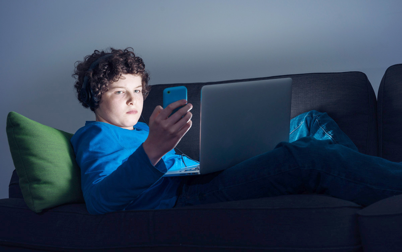 Jugendlicher schaut aufs Handy und Laptop