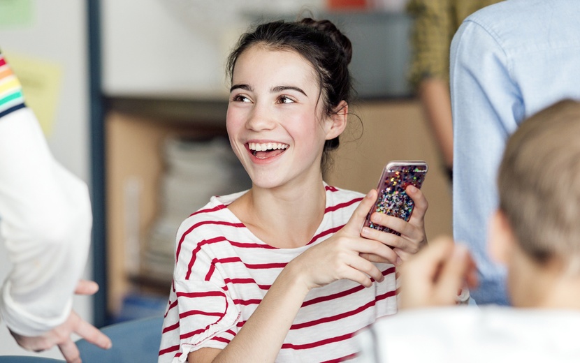 Schoolgirl laughs in the classroom and has a smartphone in her hand