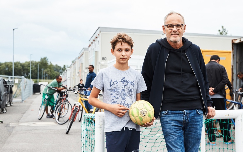 Reinhold Beckmann steht nebem einem Jungen, der einen Fußball in der Hand hält