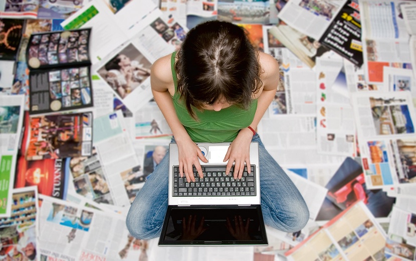 Jugendliche am Laptop inmitten von Zeitungsartikeln