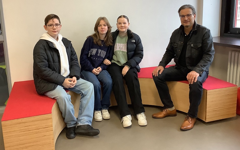 Das Foto zeigt Michael Conrads und Schüler des Ratsgymnasiums Minden, die auf einer selbstgebauten halbkreisförmigen Bank sitzen.
