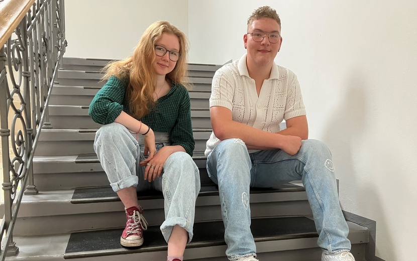 Schülerin Elli und Schüler Eddie sitzen auf einer Treppe.