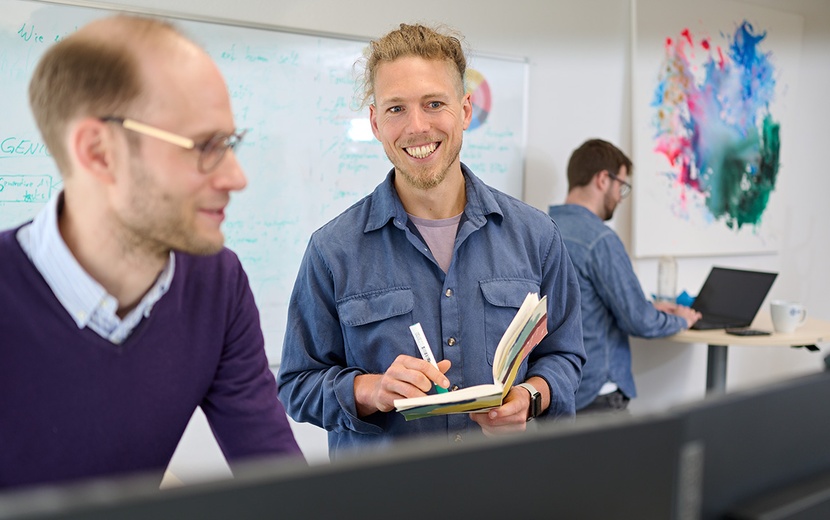 Dr. Thorben Jansen blickt mit einem Kollegen auf Monitore.