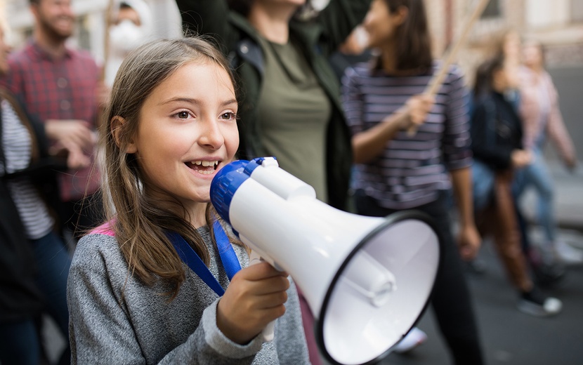 Ein Mädchen mit einem Megafon in der Hand steht in einer Menschenmenge.
