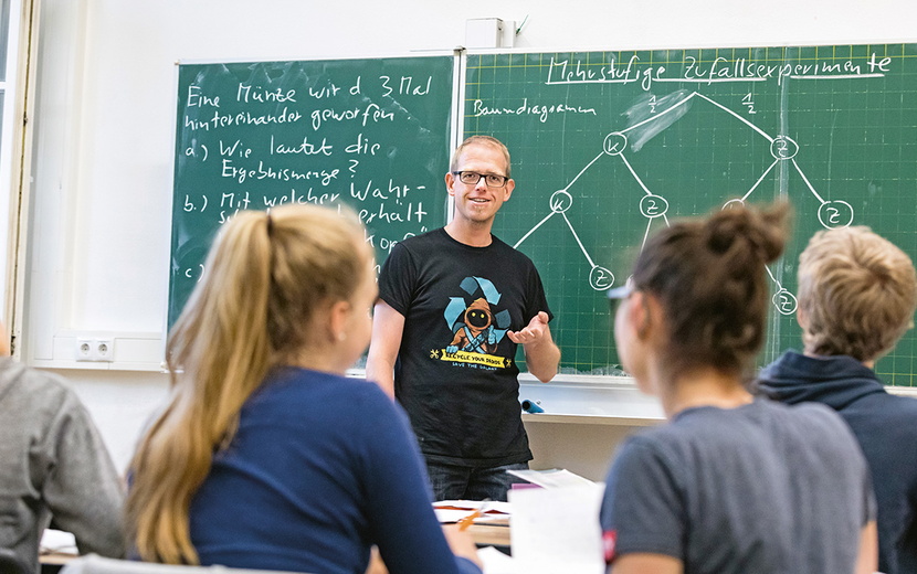 Sebastian Grab steht vorne im Klassenraum vor der Tafel.