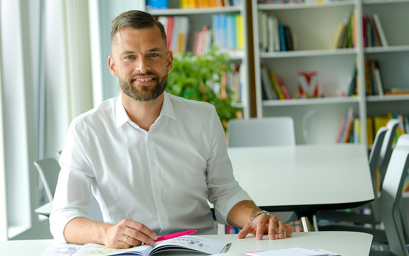 Jacob Chammon sitzt an einem Tisch. Vor ihm liegen Zeitschriften und ein Laptop.