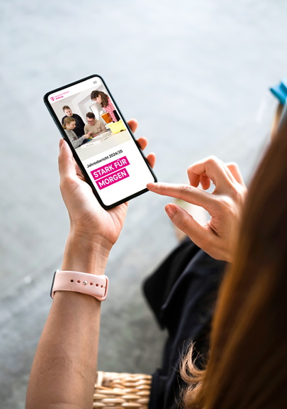 Eine Person hält ein Smartphone in der Hand. Auf dem Bildschirm ist der Jahresbericht 2024/2025 der Deutsche Telekom Stifung zu sehen. Mit