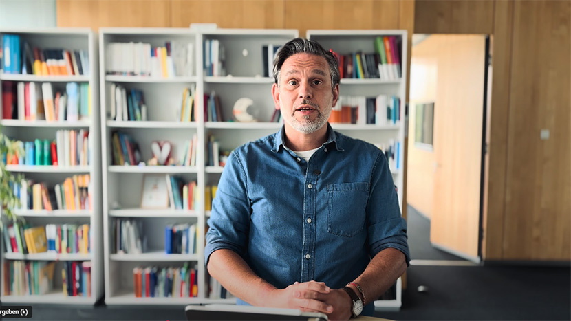 Projektleiter Benjamin Wockenfuß steht vor einem Bücherregal und schaut in die Kamera.